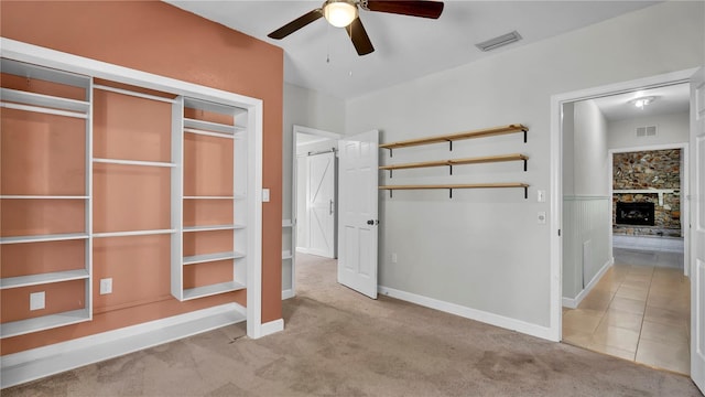 unfurnished bedroom with light carpet, a fireplace, a closet, and ceiling fan