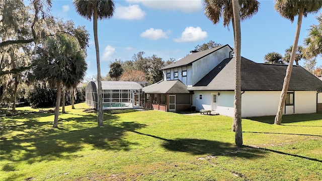 rear view of house featuring a lawn, a sunroom, and glass enclosure