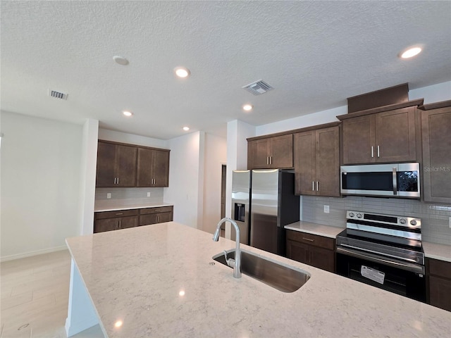 kitchen with light stone counters, dark brown cabinetry, stainless steel appliances, and sink