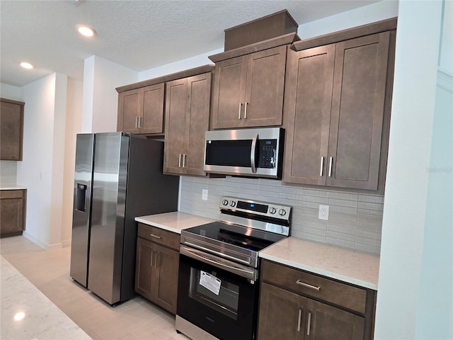 kitchen featuring stainless steel appliances, light stone countertops, backsplash, and dark brown cabinetry