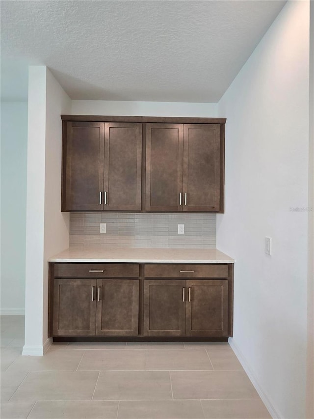 bar with dark brown cabinetry, light tile patterned floors, tasteful backsplash, and a textured ceiling