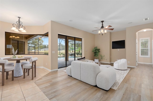 living room with ceiling fan with notable chandelier and light hardwood / wood-style flooring