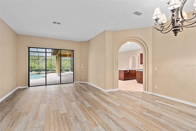 spare room with an inviting chandelier and light hardwood / wood-style floors