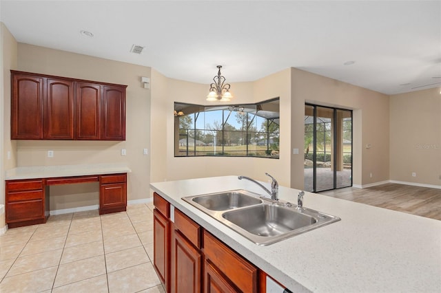 kitchen with sink, built in desk, hanging light fixtures, light tile patterned floors, and a notable chandelier