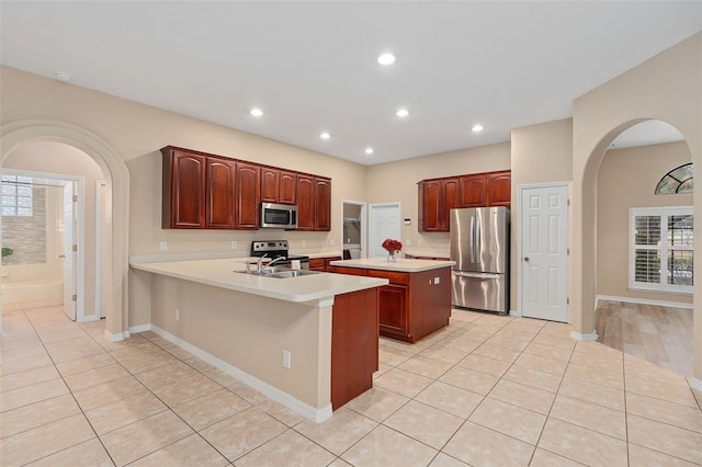 kitchen with appliances with stainless steel finishes, a center island, light tile patterned floors, and kitchen peninsula