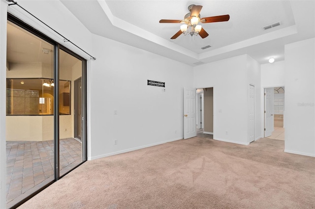 carpeted empty room featuring ceiling fan and a raised ceiling