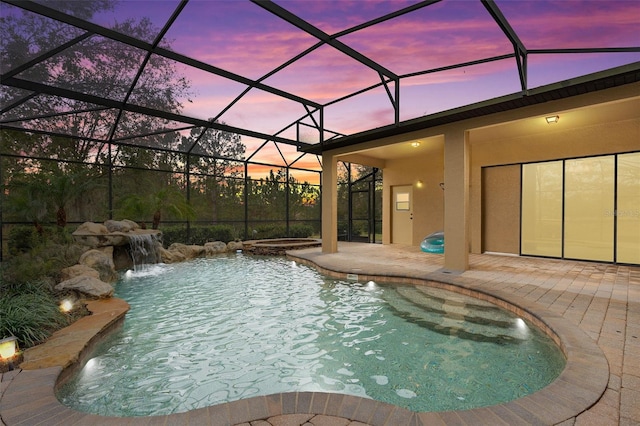 pool at dusk with an in ground hot tub, pool water feature, a lanai, and a patio