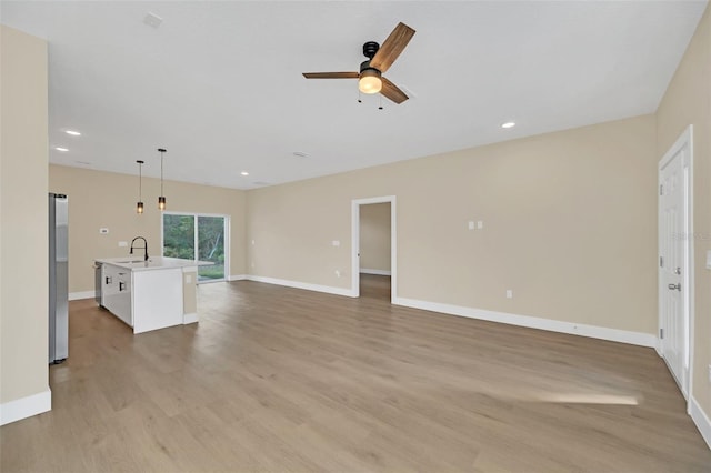 unfurnished living room with ceiling fan, sink, and light wood-type flooring