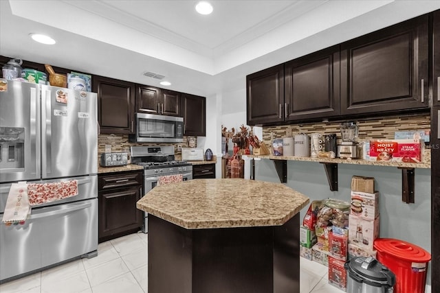 kitchen with dark brown cabinetry, a kitchen bar, crown molding, appliances with stainless steel finishes, and decorative backsplash