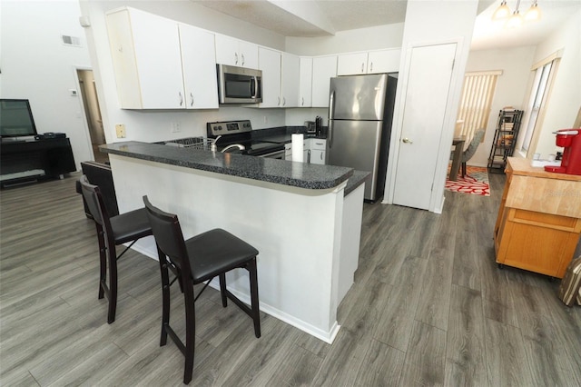 kitchen with appliances with stainless steel finishes, white cabinets, dark hardwood / wood-style flooring, and kitchen peninsula