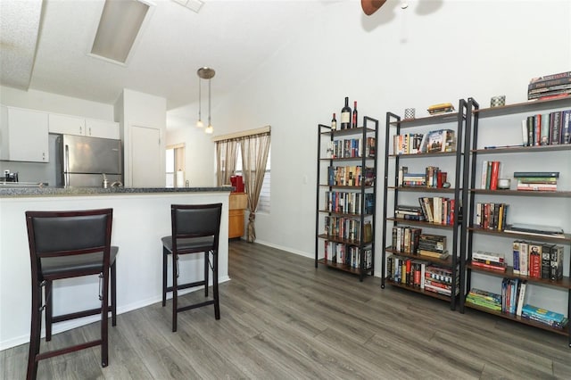 kitchen featuring dark wood-type flooring, a breakfast bar area, white cabinetry, decorative light fixtures, and stainless steel fridge