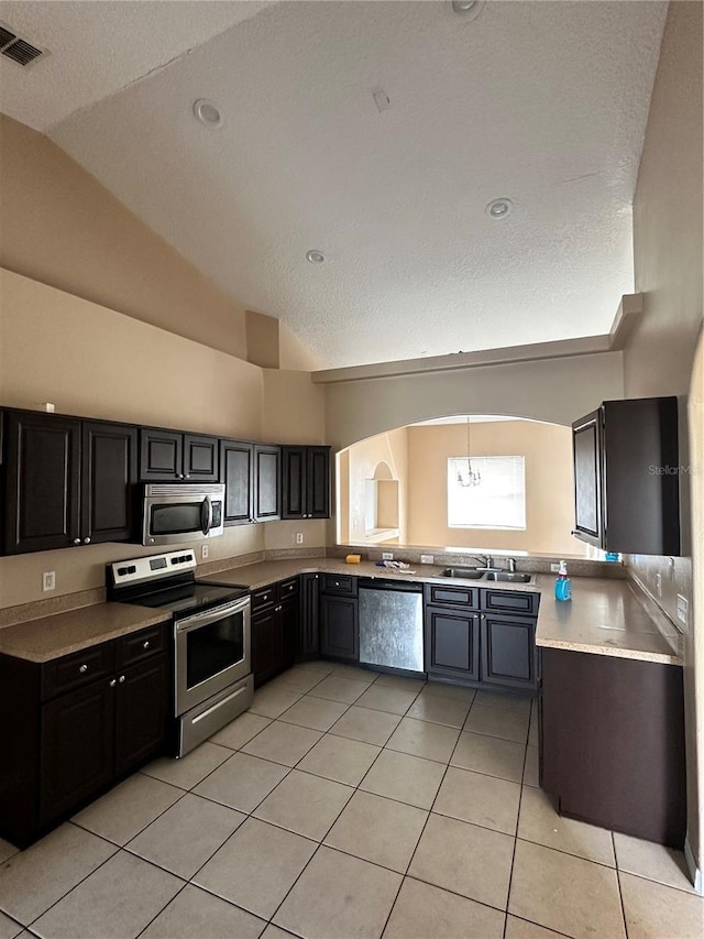 kitchen featuring vaulted ceiling, sink, light tile patterned floors, stainless steel appliances, and a textured ceiling