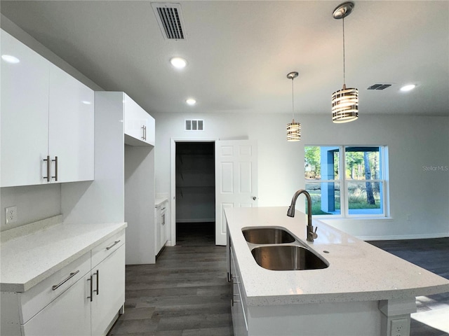 kitchen with decorative light fixtures, white cabinetry, an island with sink, sink, and light stone countertops