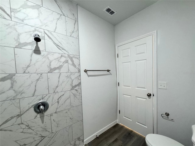 bathroom featuring hardwood / wood-style flooring, toilet, and tiled shower