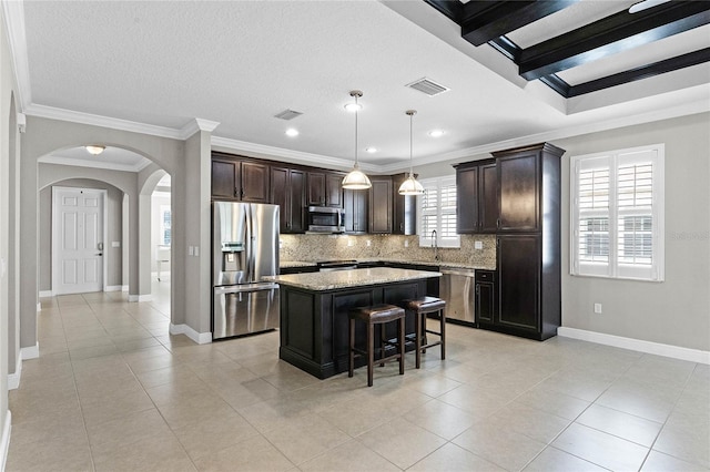 kitchen with appliances with stainless steel finishes, a breakfast bar, pendant lighting, tasteful backsplash, and a center island