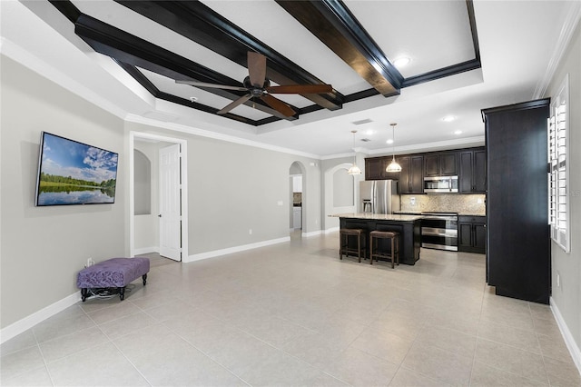 kitchen featuring appliances with stainless steel finishes, a breakfast bar, decorative light fixtures, an island with sink, and a raised ceiling