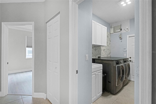 clothes washing area featuring cabinets, light tile patterned flooring, and washing machine and clothes dryer