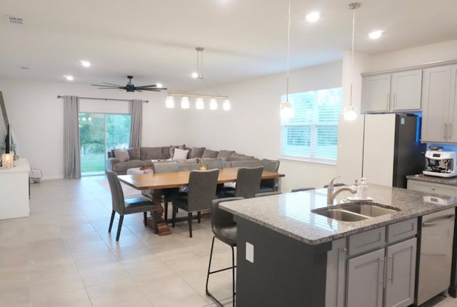 kitchen with sink, light stone countertops, a center island with sink, decorative light fixtures, and stainless steel dishwasher