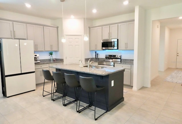 kitchen with sink, a breakfast bar area, stainless steel appliances, light stone counters, and an island with sink