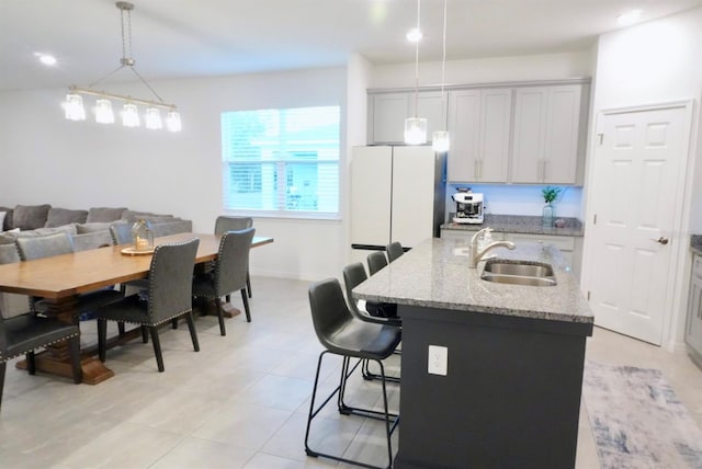 kitchen with pendant lighting, sink, a kitchen breakfast bar, light stone counters, and a center island with sink