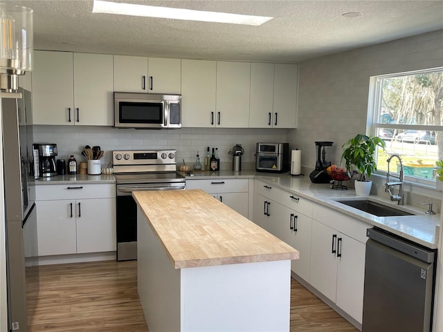 kitchen featuring light wood finished floors, a center island, butcher block counters, appliances with stainless steel finishes, and a sink