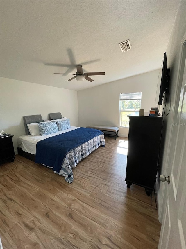 bedroom featuring a ceiling fan, wood finished floors, visible vents, and a textured ceiling