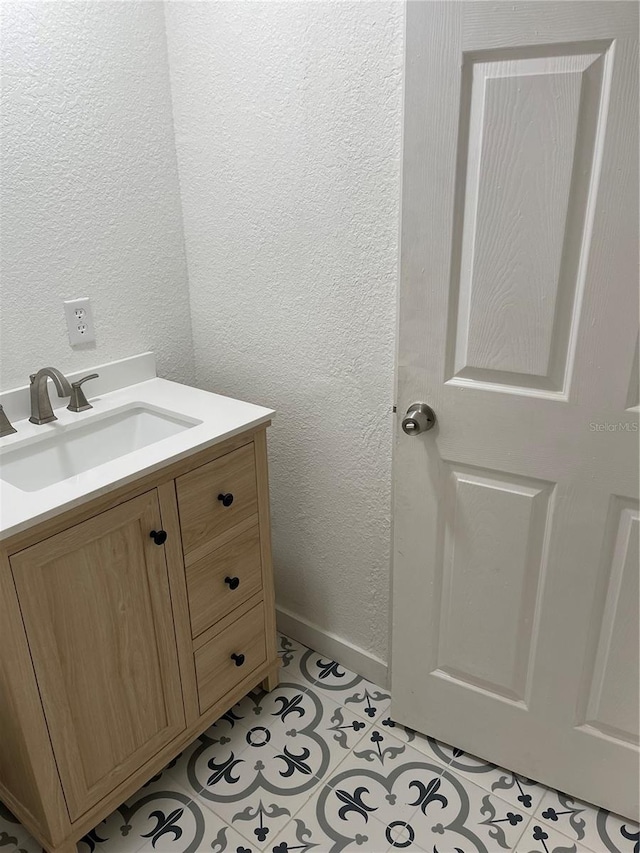 bathroom featuring tile patterned floors, vanity, baseboards, and a textured wall