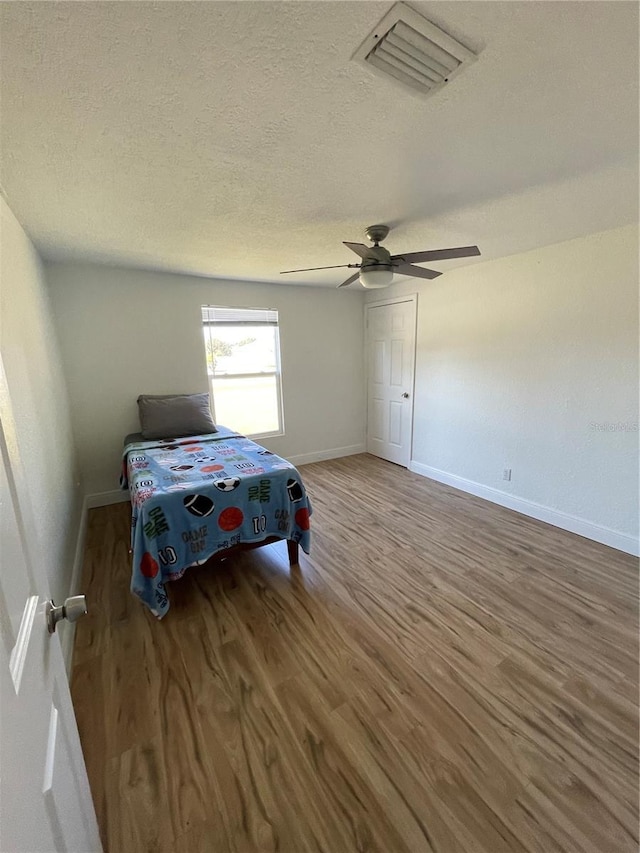 bedroom with visible vents, a textured ceiling, wood finished floors, baseboards, and ceiling fan