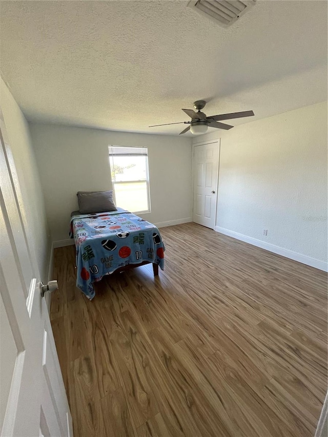 bedroom featuring visible vents, a ceiling fan, a textured ceiling, wood finished floors, and baseboards