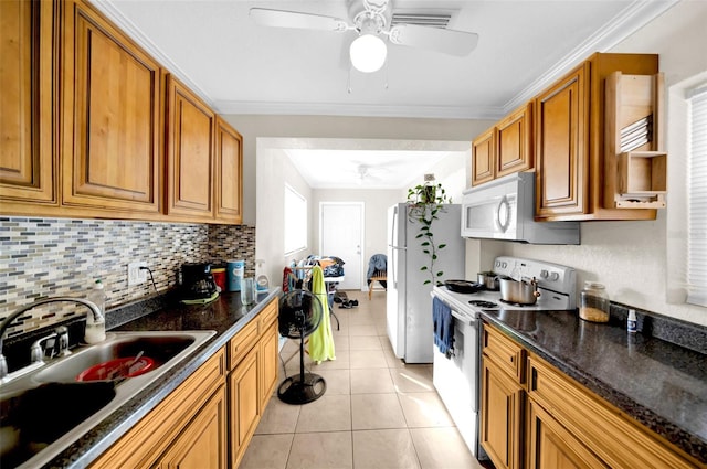 kitchen with light tile patterned flooring, sink, dark stone countertops, crown molding, and white appliances