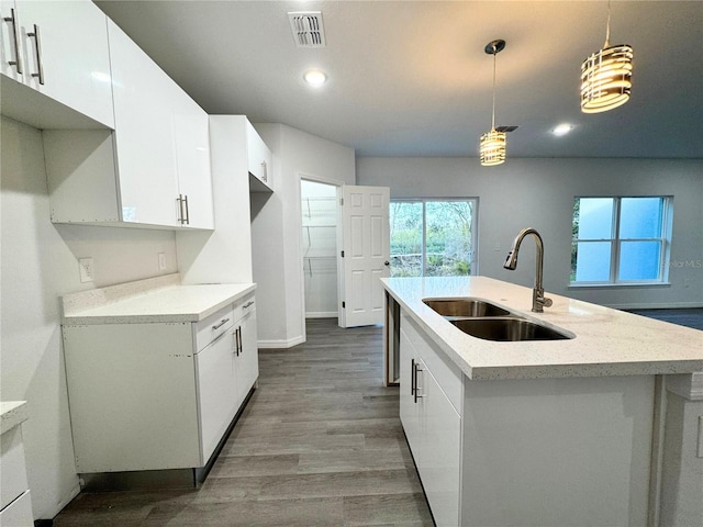 kitchen with sink, white cabinetry, wood-type flooring, decorative light fixtures, and an island with sink