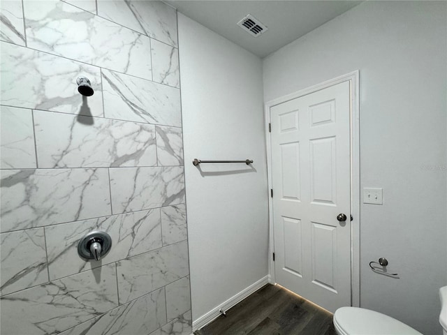 bathroom with hardwood / wood-style floors, a tile shower, and toilet