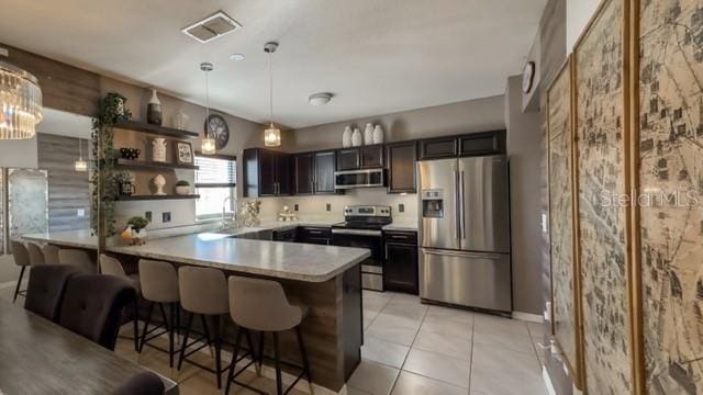 kitchen featuring pendant lighting, a kitchen bar, light tile patterned floors, kitchen peninsula, and stainless steel appliances