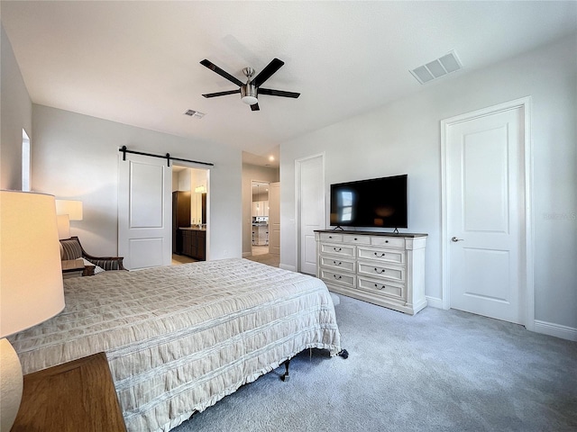 bedroom with ensuite bathroom, a barn door, carpet, and ceiling fan