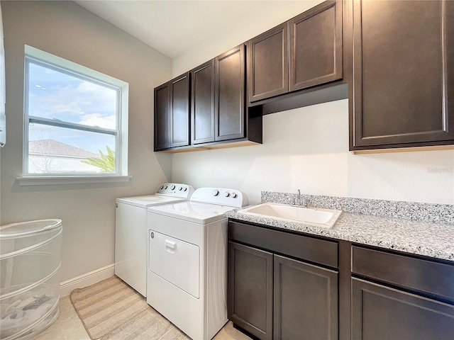 clothes washing area with sink, light tile patterned floors, washing machine and dryer, and cabinets