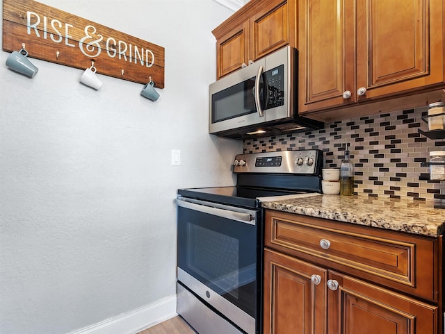 kitchen featuring light stone counters, stainless steel appliances, light hardwood / wood-style floors, and backsplash