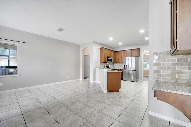 kitchen featuring light tile patterned floors, kitchen peninsula, stainless steel appliances, light stone countertops, and backsplash