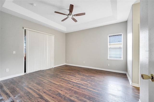 unfurnished bedroom with a tray ceiling, dark wood-type flooring, and ceiling fan