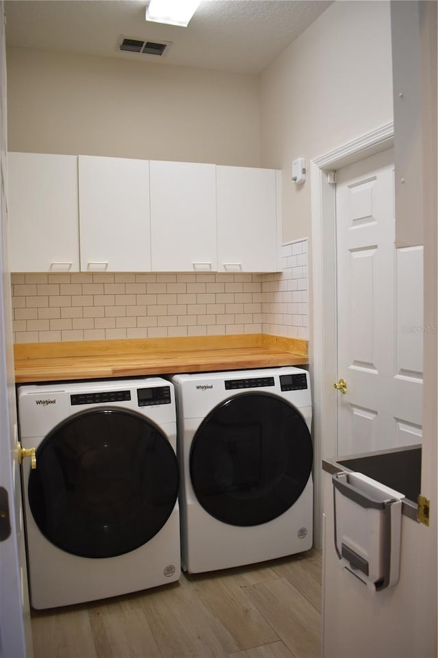 laundry area featuring light hardwood / wood-style floors, washing machine and dryer, and cabinets