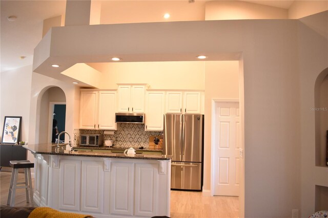 kitchen featuring white cabinetry, decorative backsplash, stainless steel appliances, and dark stone countertops