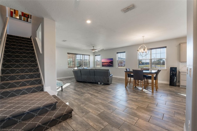 living room with ceiling fan with notable chandelier and a textured ceiling