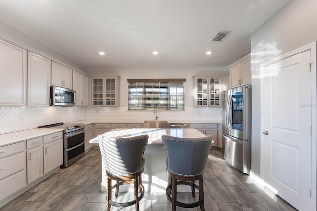 kitchen with gray cabinets, a kitchen island, appliances with stainless steel finishes, tasteful backsplash, and sink