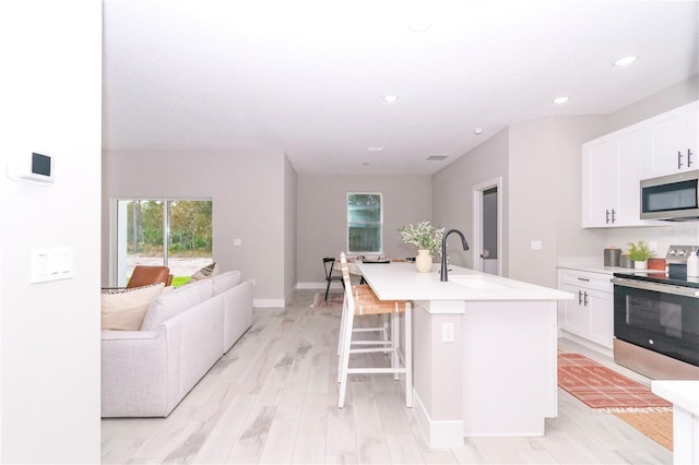 kitchen featuring white cabinetry, an island with sink, appliances with stainless steel finishes, and a breakfast bar area