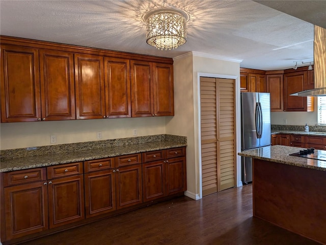 kitchen with exhaust hood, dark hardwood / wood-style flooring, light stone counters, and stainless steel refrigerator