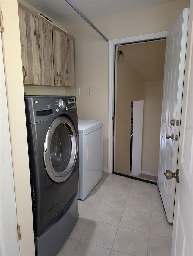 clothes washing area with separate washer and dryer, light tile patterned floors, and cabinets