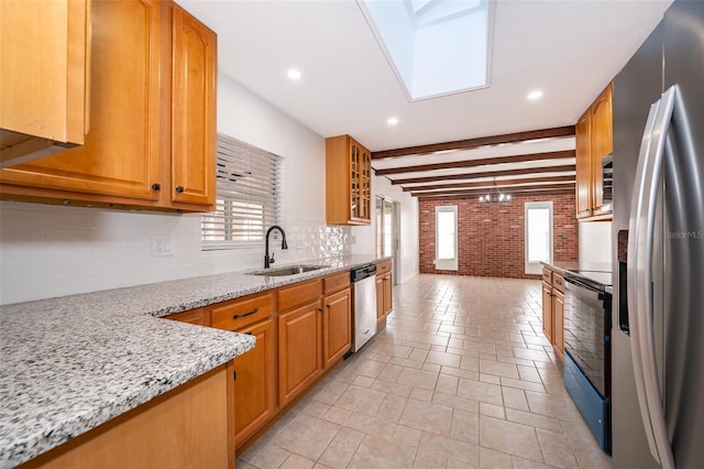 kitchen with sink, brick wall, appliances with stainless steel finishes, a healthy amount of sunlight, and light stone countertops