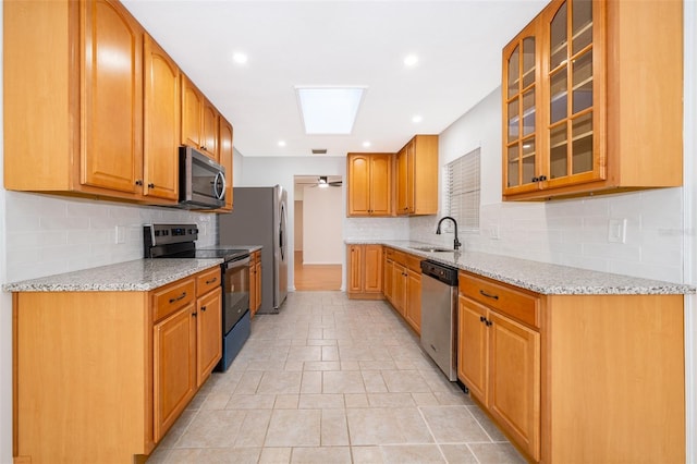 kitchen with a skylight, tasteful backsplash, sink, stainless steel appliances, and light stone countertops