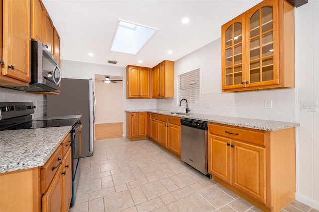 kitchen featuring sink, light stone counters, a skylight, stainless steel appliances, and decorative backsplash