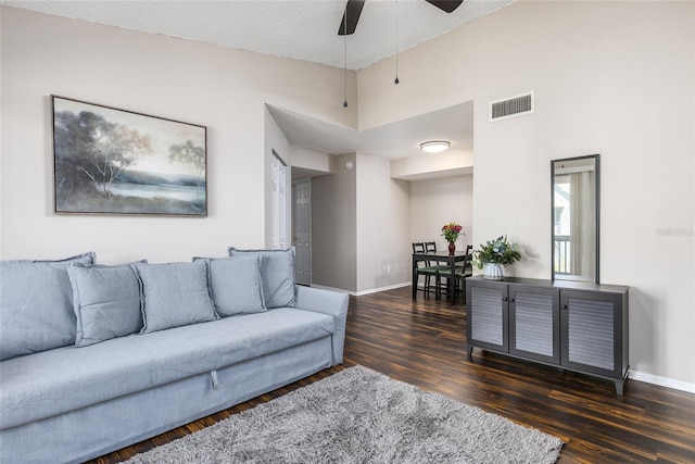 living room featuring ceiling fan, dark hardwood / wood-style floors, a textured ceiling, and a towering ceiling