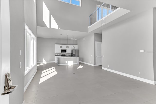 unfurnished living room with a healthy amount of sunlight, a towering ceiling, and light tile patterned floors